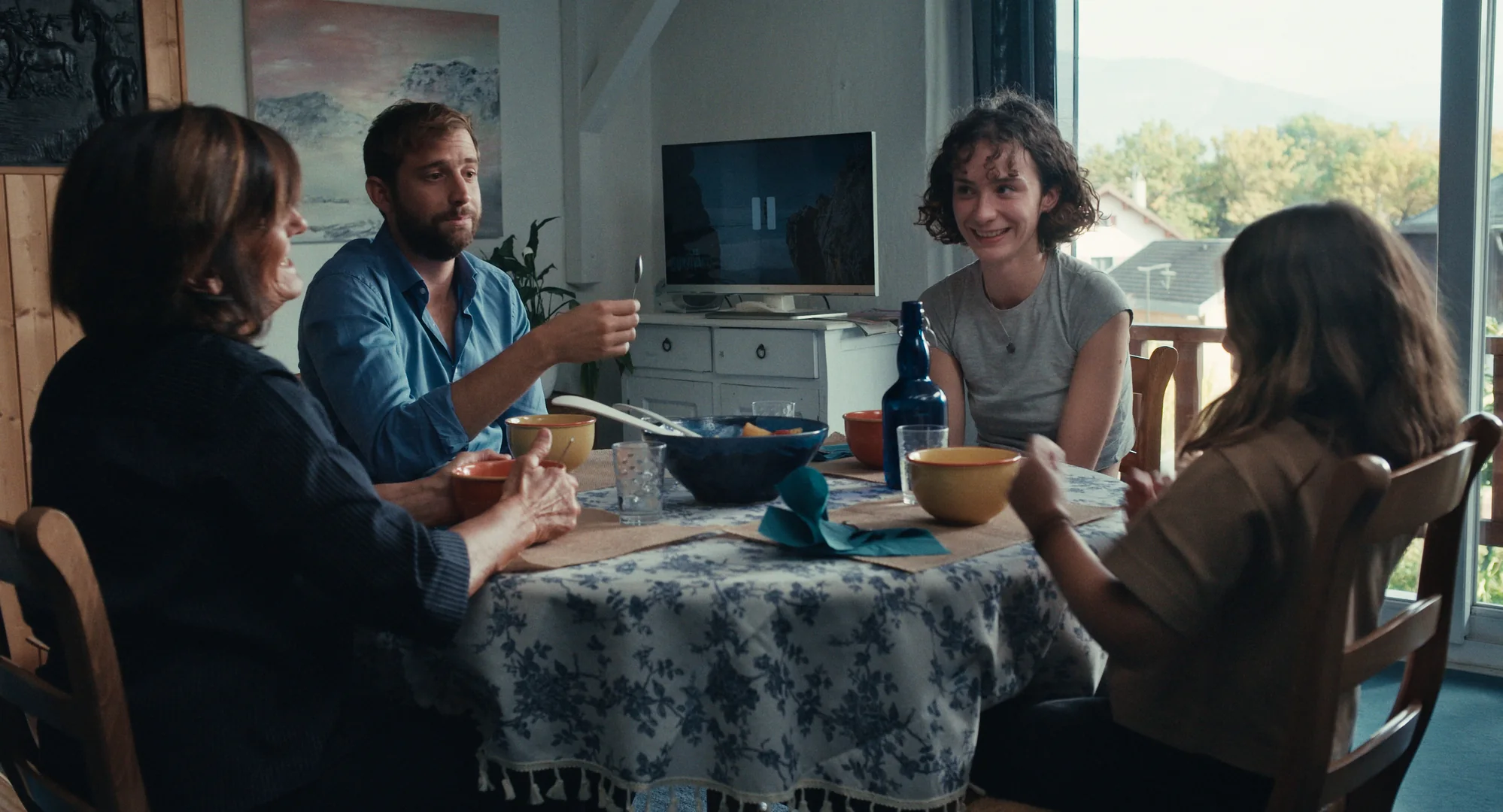Parasocial, un repas de famille. Au fond de la pièce, une télévision est en pause.